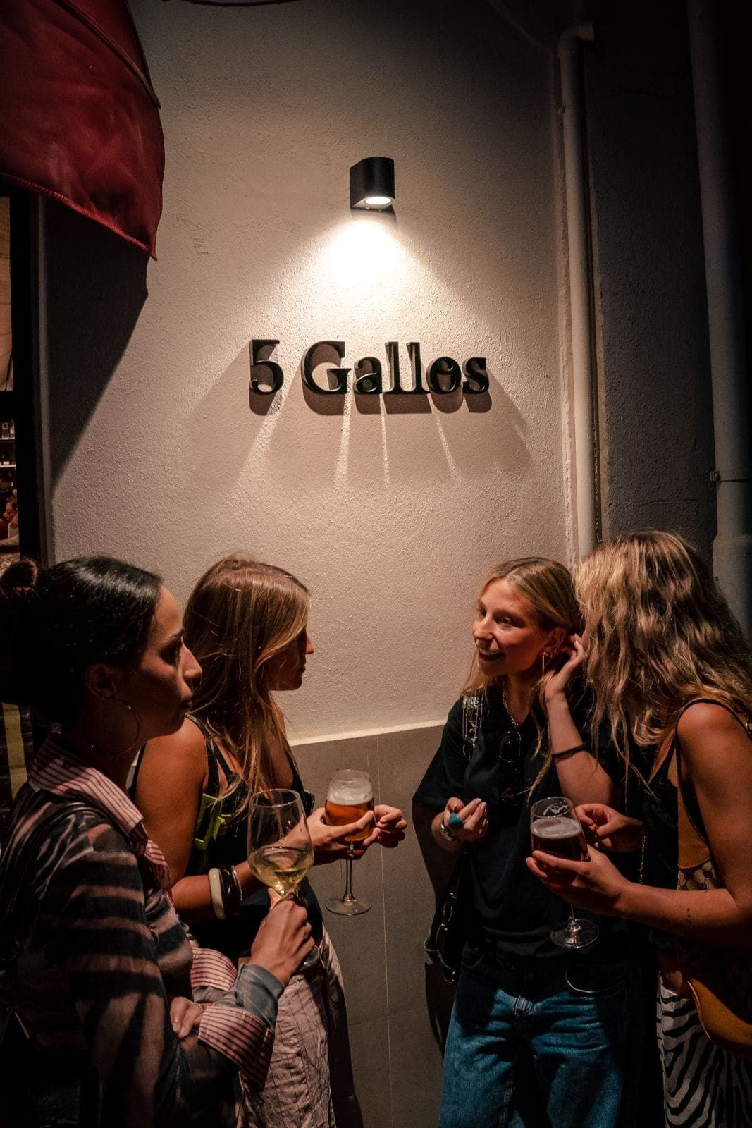 Cuatro amigas charlan con una copa bajo el letrero de 5 Gallos