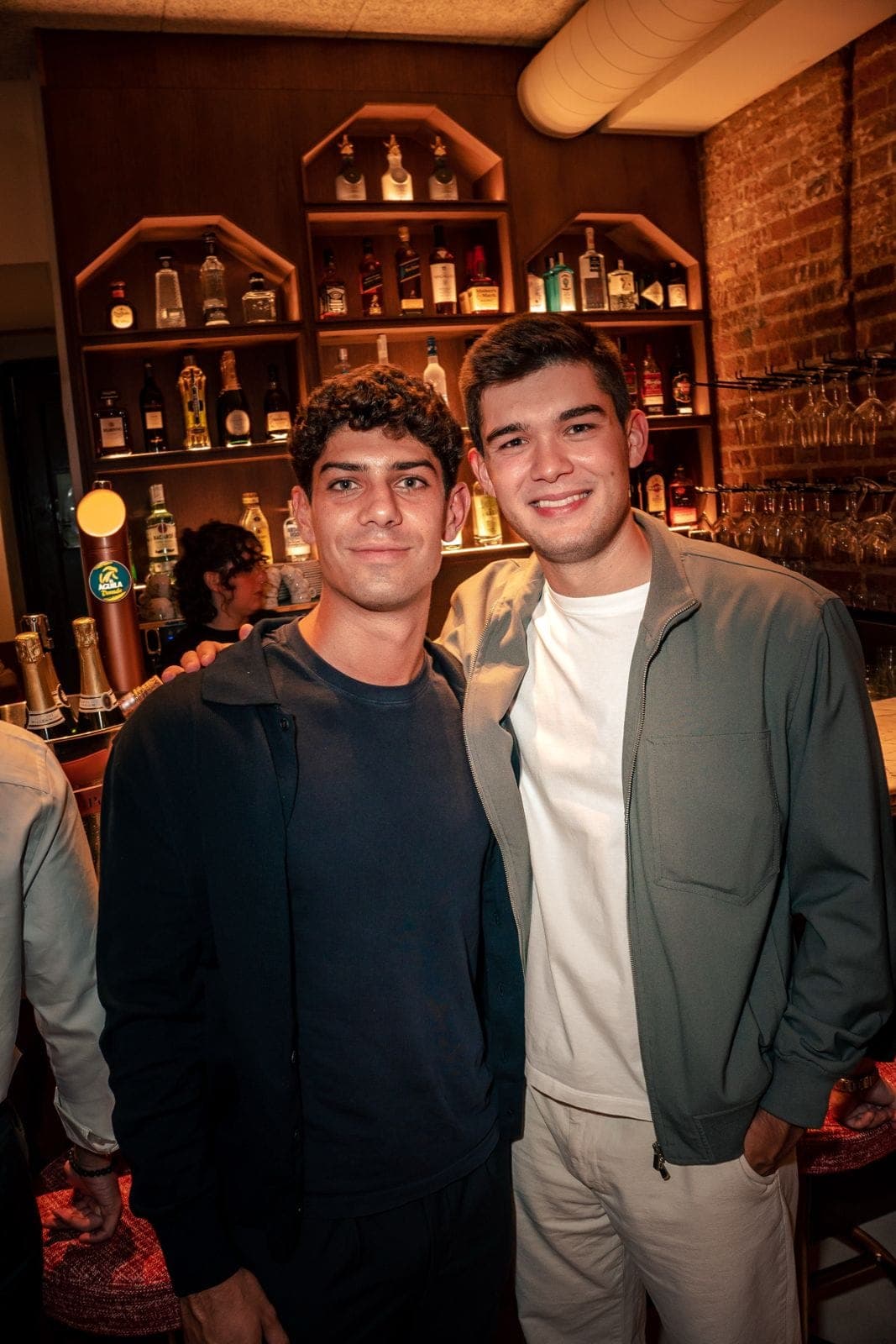 Dos amigos sonríen frente a la contrabarra de botellas