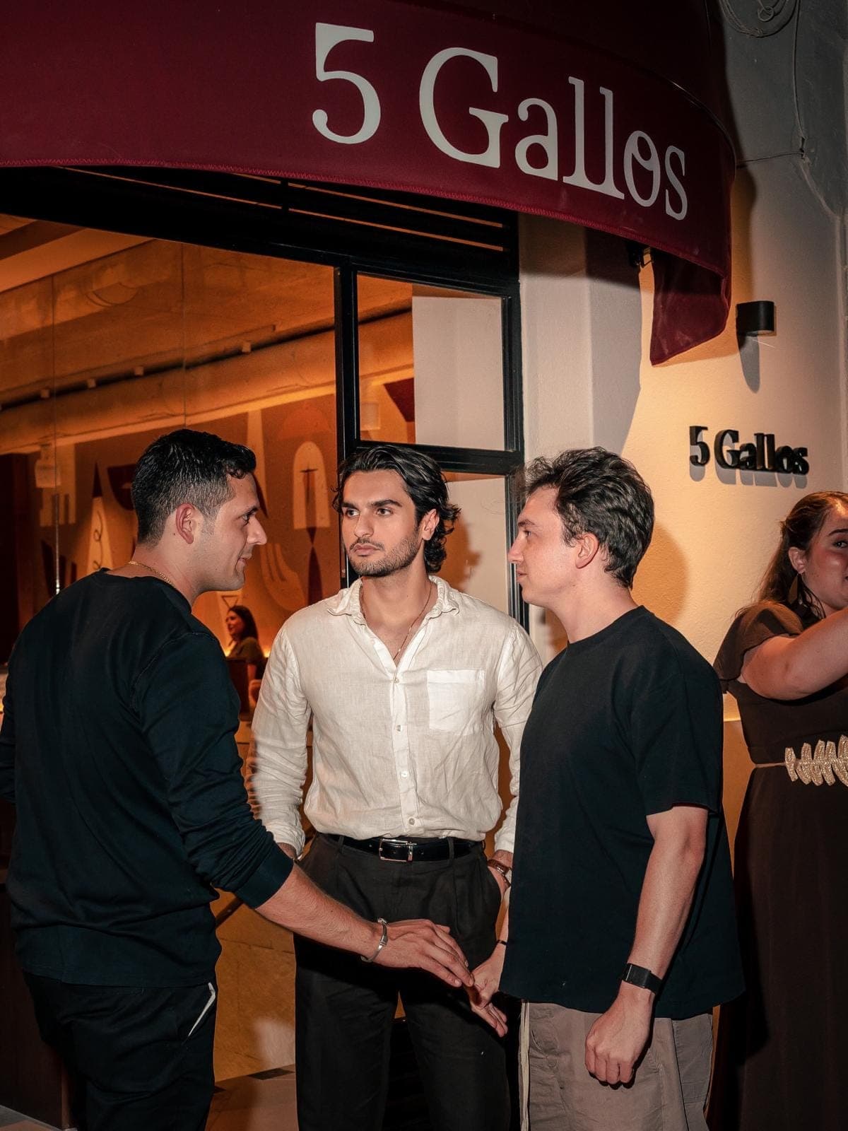 Tres amigos se saludan en la entrada, bajo el toldo vino