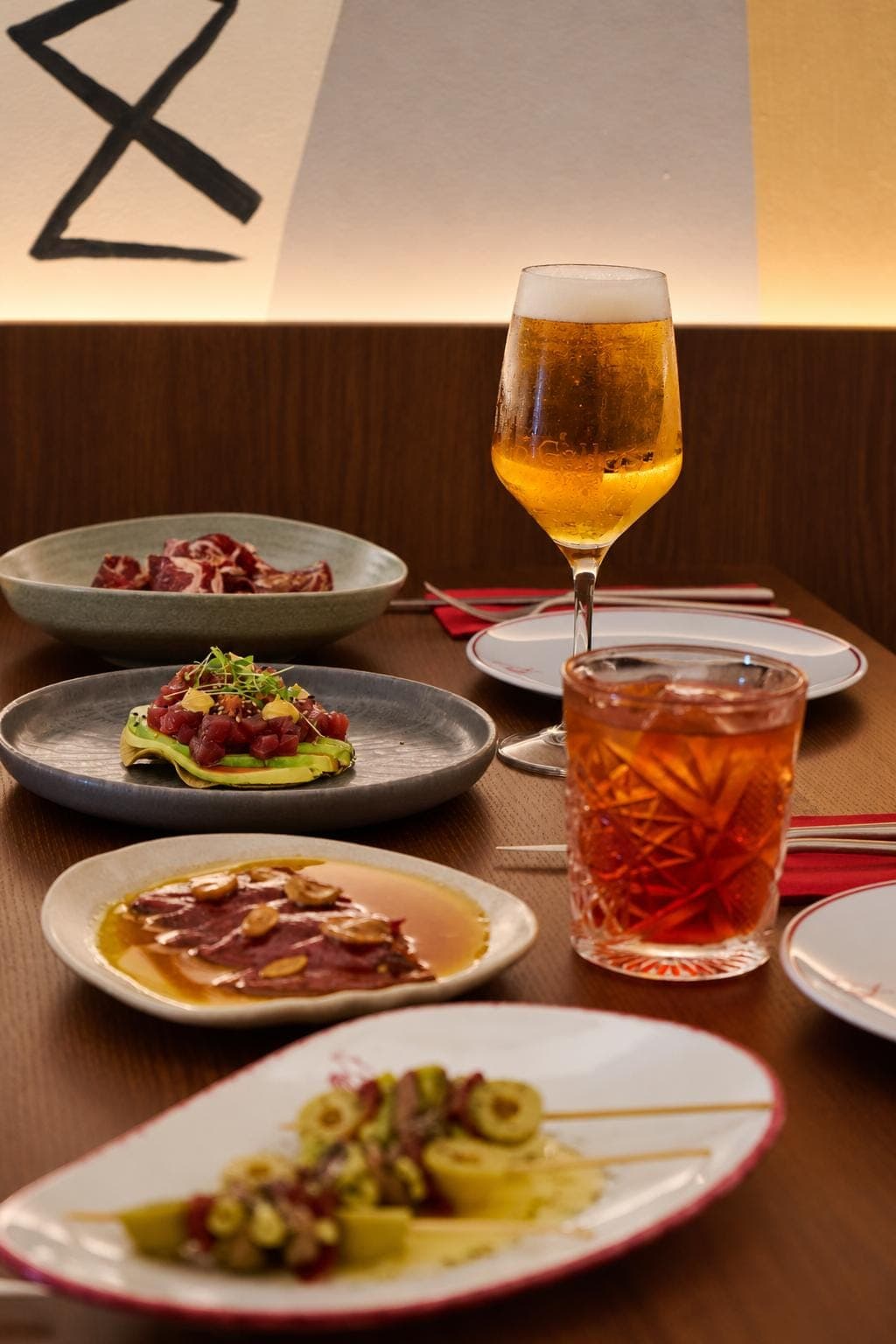 Platos para compartir —jamón, atún sobre aguacate y gildas— con una caña y un cóctel