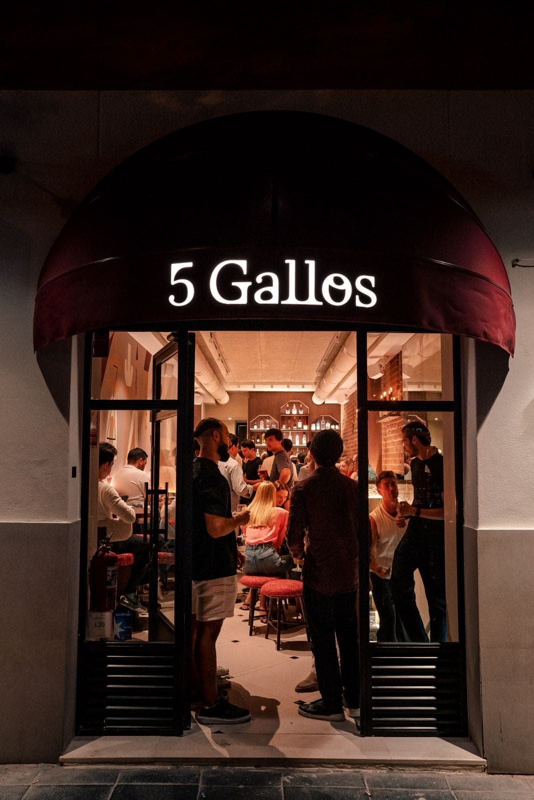 La puerta abierta de 5 Gallos de noche, con el toldo iluminado y la sala llena